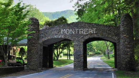 A stone archway with the word MONTREAT leads over a two-lane road surrounded by green trees and mountains in the background.