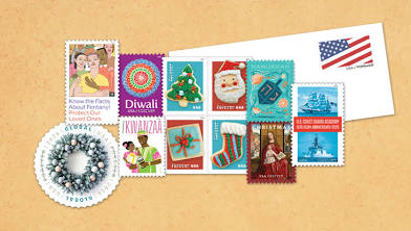 A collection of colorful postage stamps featuring holiday themes, a wreath, and an American flag, arranged on a tan background next to a white envelope.