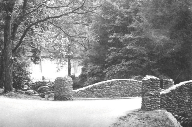 A stone-walled bridge crossing a small stream in a wooded park.