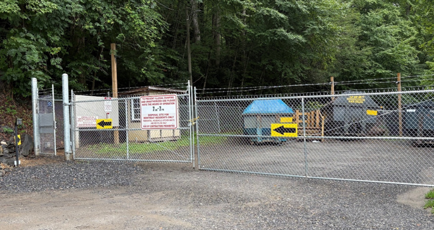 A fenced-in waste disposal site with large dumpsters and signs indicating resident-only access and operating hours.
