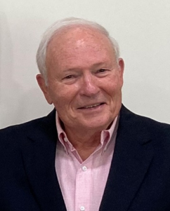 Headshot of an older man with white hair wearing a navy blue blazer over a pink button-down shirt.